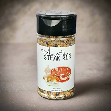 A clear plastic jar labeled Austin Steak Rub 🥩, featuring images of steak, garlic, and onions, sits on a neutral surface against a light beige background.